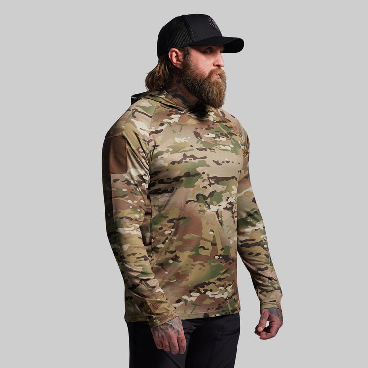 Man wearing a camouflage long-sleeve shirt and black cap on a gray background