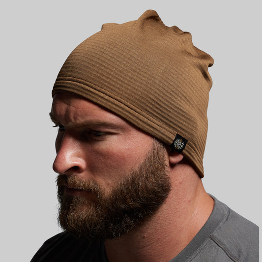Man wearing a brown beanie with a brand logo on a gray background