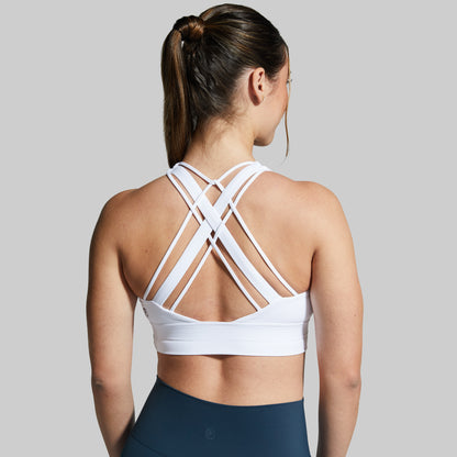 Woman wearing a white sports bra with criss-cross straps on a gray background