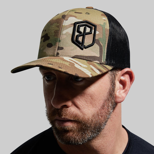 Man wearing a camouflage trucker hat with a logo on a gray background