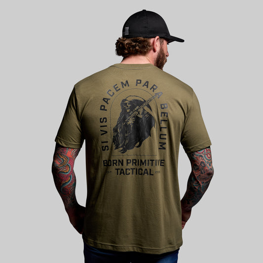 Man wearing a green t-shirt with tactical design and text, standing against a gray background