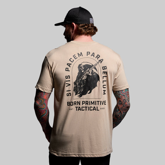 Man wearing a beige t-shirt with a graphic design and text, standing against a plain background