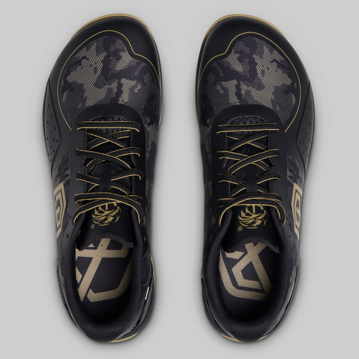 A pair of athletic sneakers shown from a top-down view on a light gray background. The shoes feature a dark gray and black camouflage pattern with metallic gold accents on the laces, lining, and logo details.