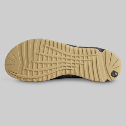 A close-up of a shoe's tan and black outsole, showing the tread pattern and heel detail, set against a solid gray background.