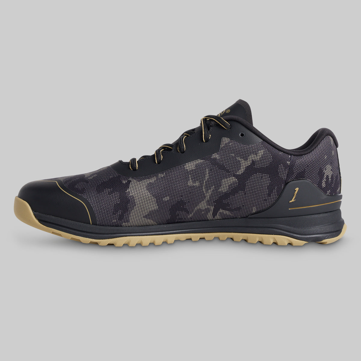 A low-top athletic shoe shown in a side profile on a solid gray background. The shoe features a dark gray and black camouflage pattern upper, black laces, a black toe cap, and a light tan outsole.