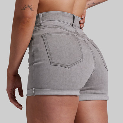 A close-up back view of a model wearing light gray denim shorts with a rolled hem and a single back pocket, shown against a solid gray background.