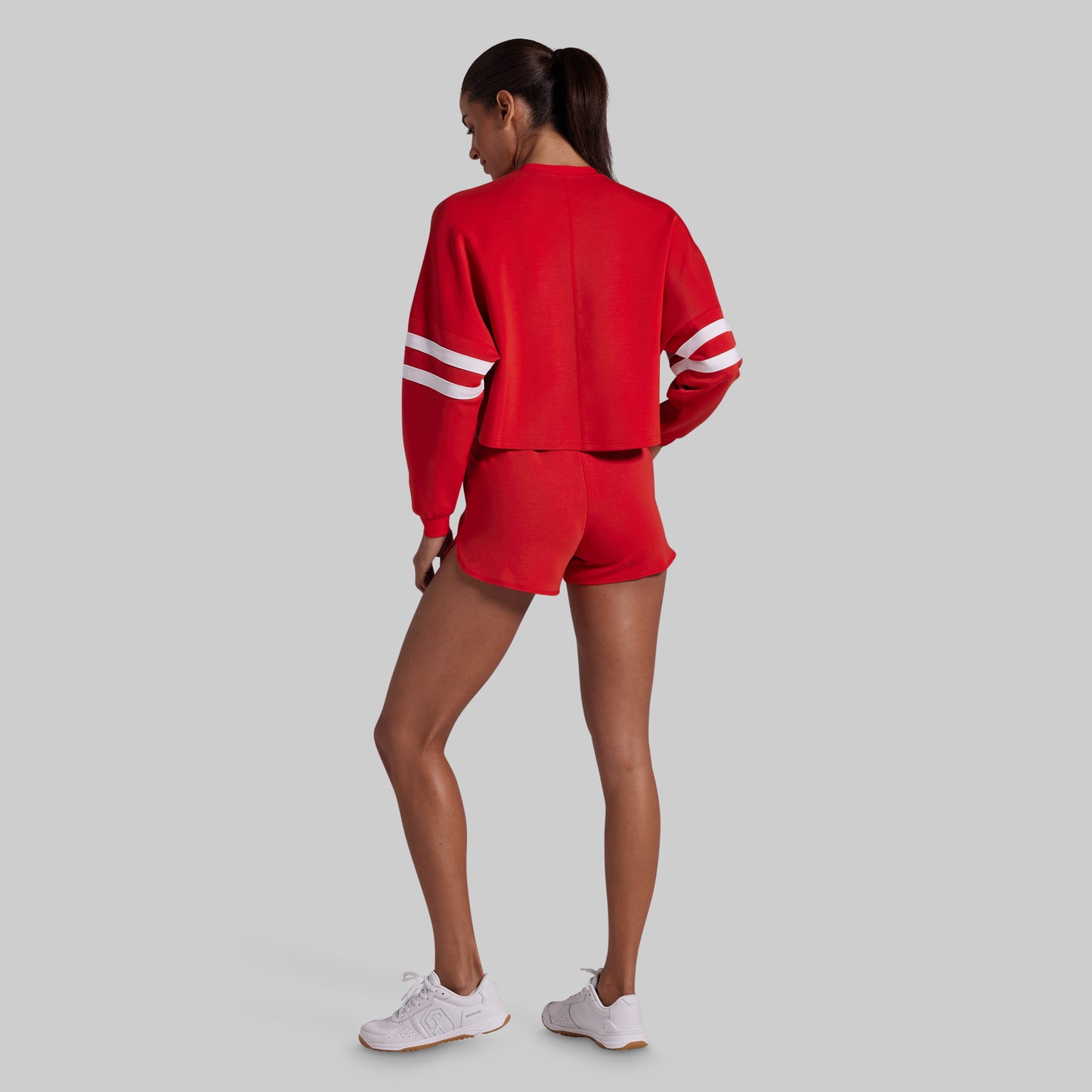 A woman wearing a red athletic tracksuit with white stripes on the sleeves, shown from the back against a solid gray background.
