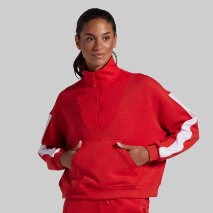 A woman modeling a bright red athletic zip-up jacket with white sleeve stripes, posed against a solid light gray background.