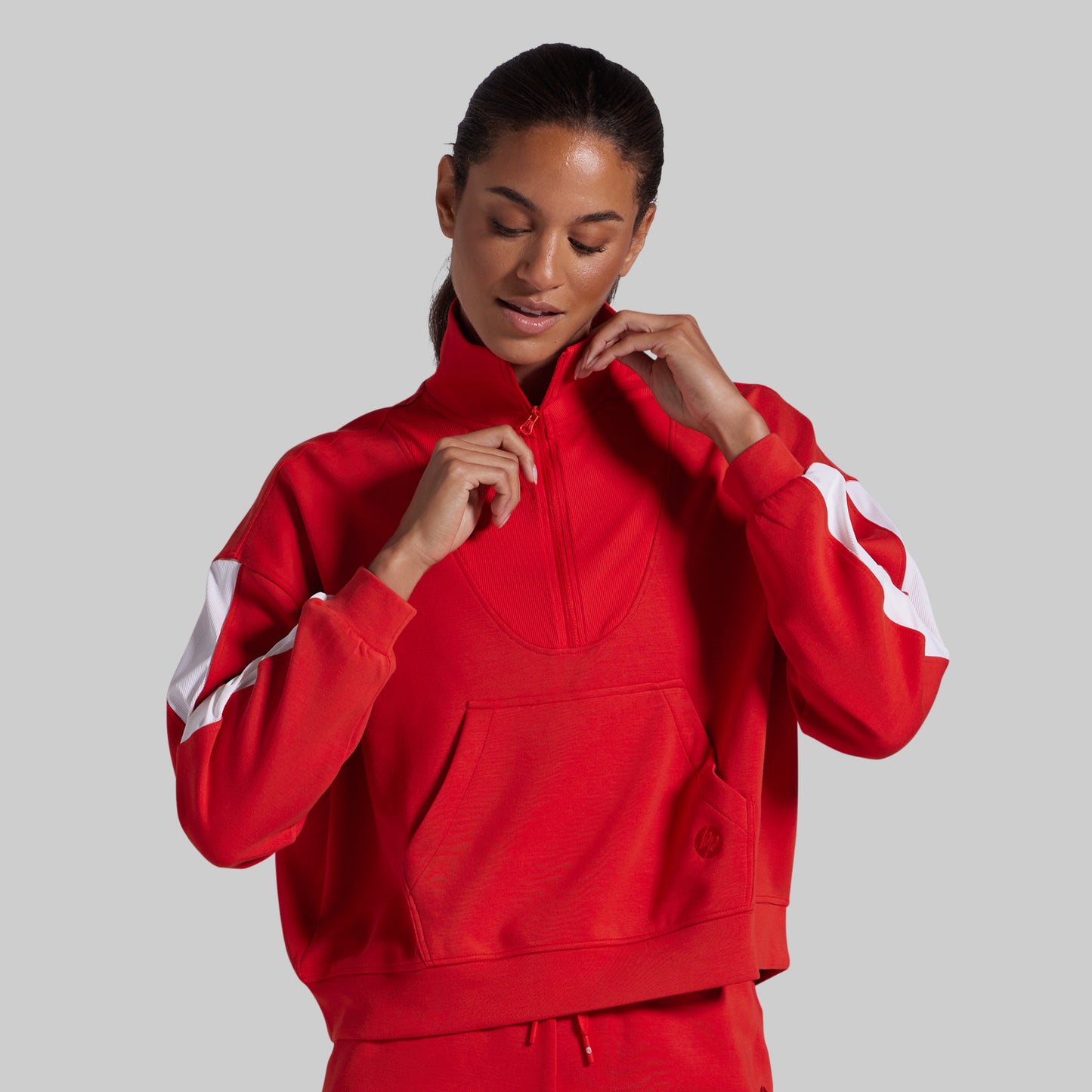 A woman wearing a bright red half-zip sweatshirt with white sleeve stripes, posing against a solid gray background.