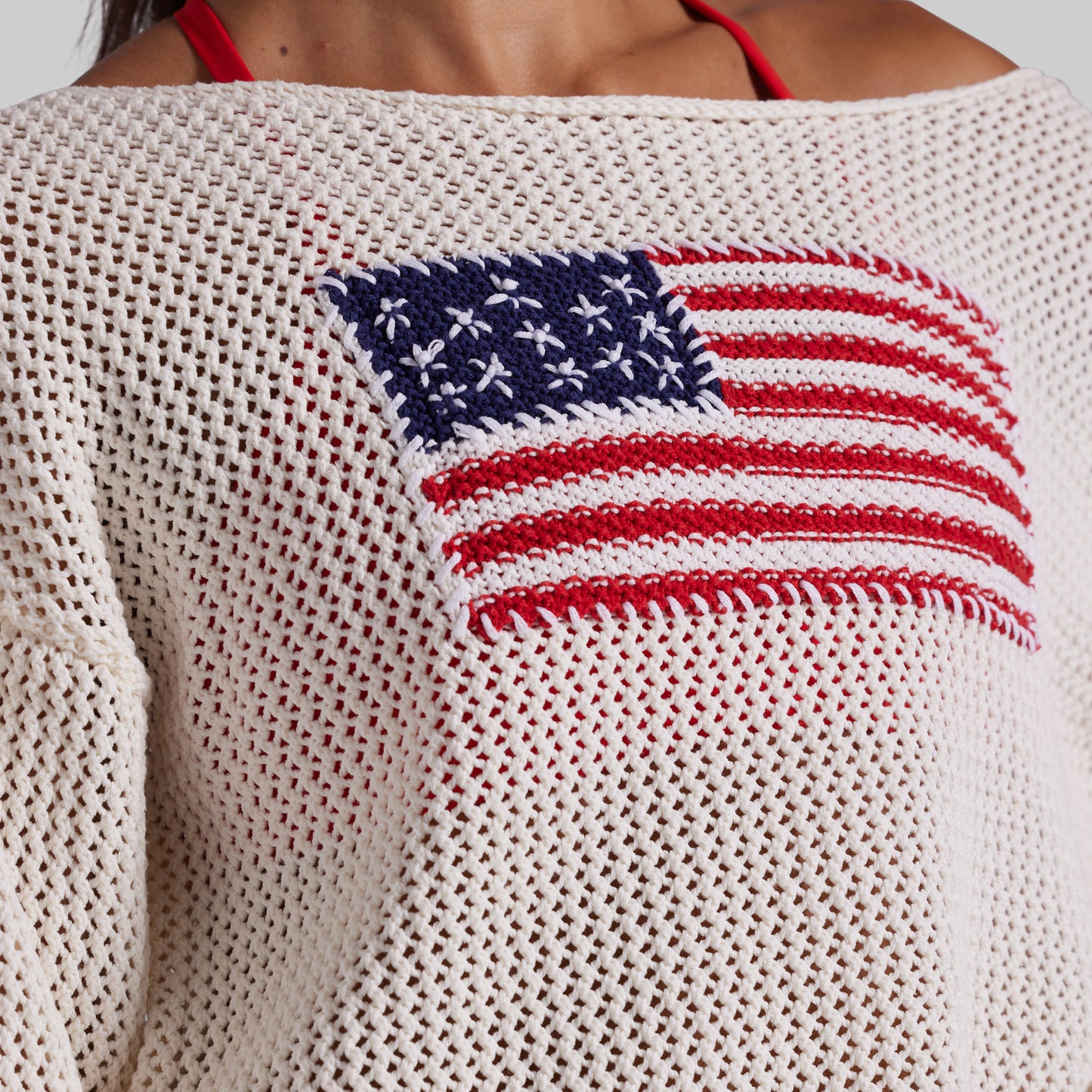 Close-up of a cream-colored knit sweater with a red, white, and blue American flag motif on the chest, worn by a model.