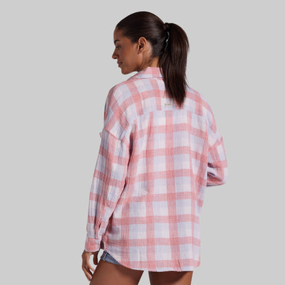 A woman shown from the back wearing an oversized pink and white plaid button-up shirt, paired with denim shorts, against a solid gray background.