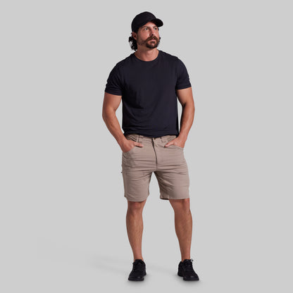 A man modeling a black short-sleeve crewneck t-shirt and beige cargo shorts against a solid gray background.