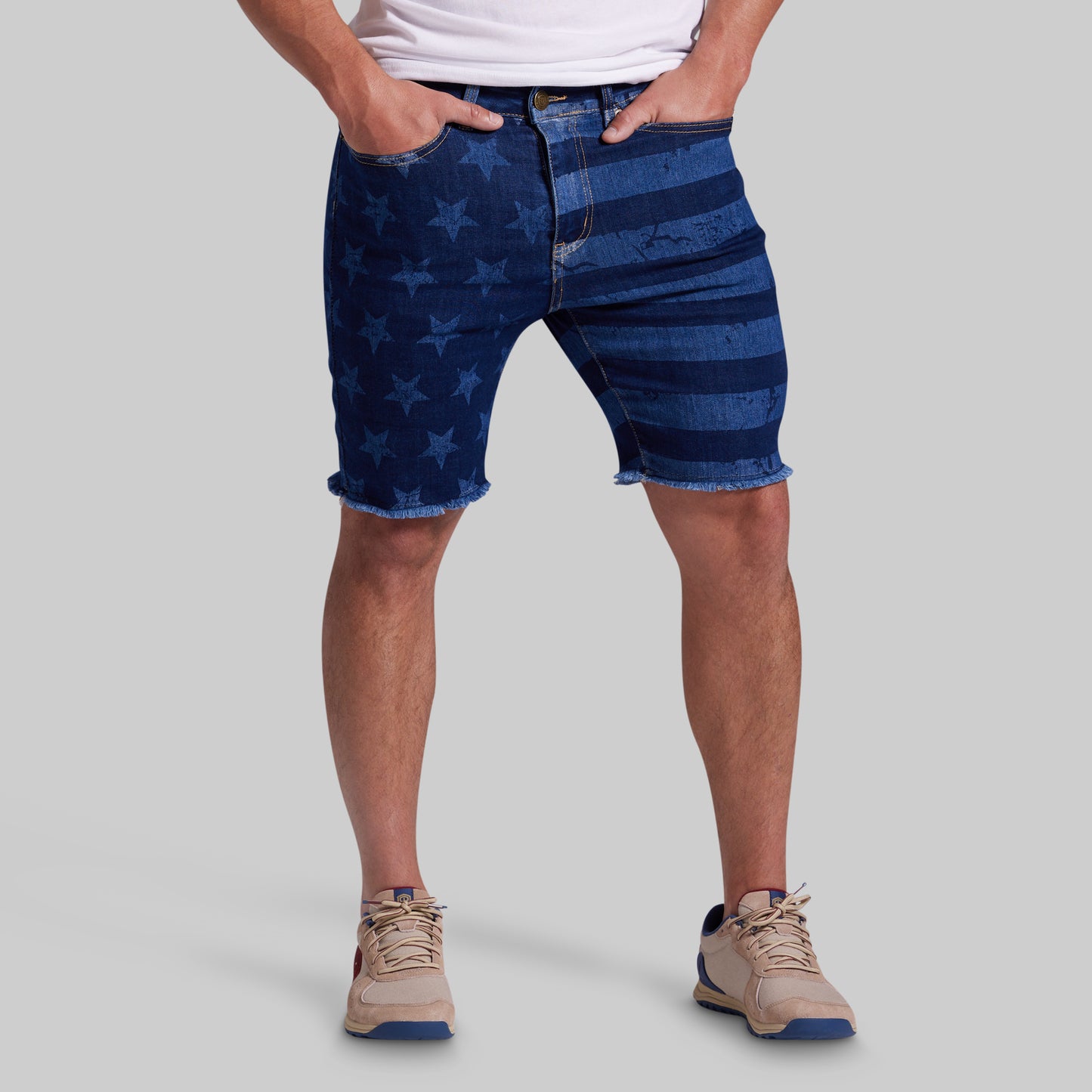 A person wearing blue denim shorts with a faded star pattern on one leg and horizontal stripe patterns on the other, paired with a white t-shirt and beige sneakers, against a solid gray background.