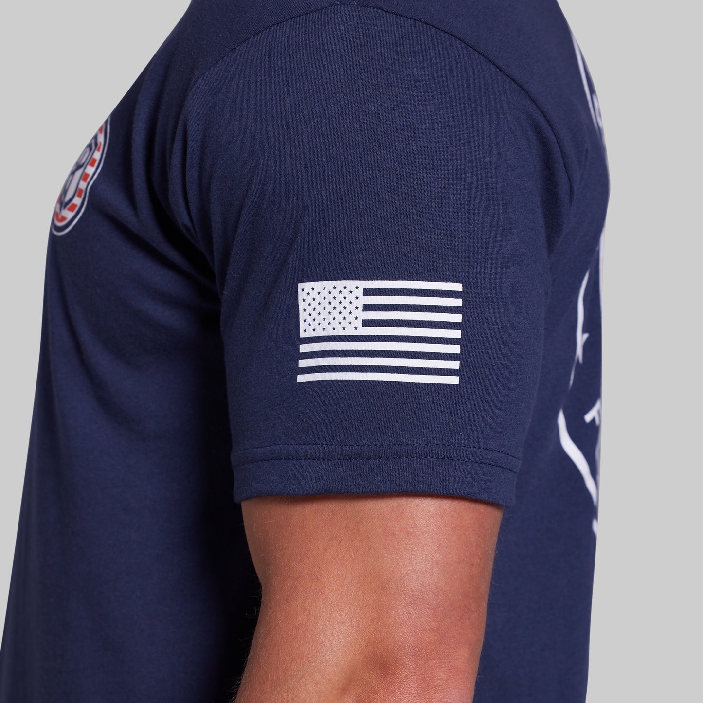 Close-up of a navy blue short-sleeve athletic T-shirt worn by a model, showing a white American flag graphic on the left sleeve.