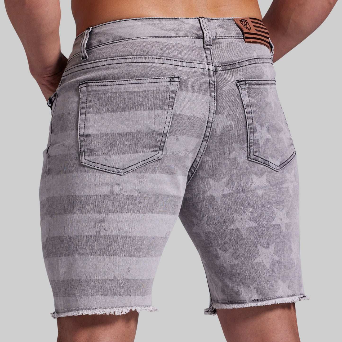 Gray denim shorts with a faded horizontal stripe and star pattern, shown from the back on a model against a light gray background.