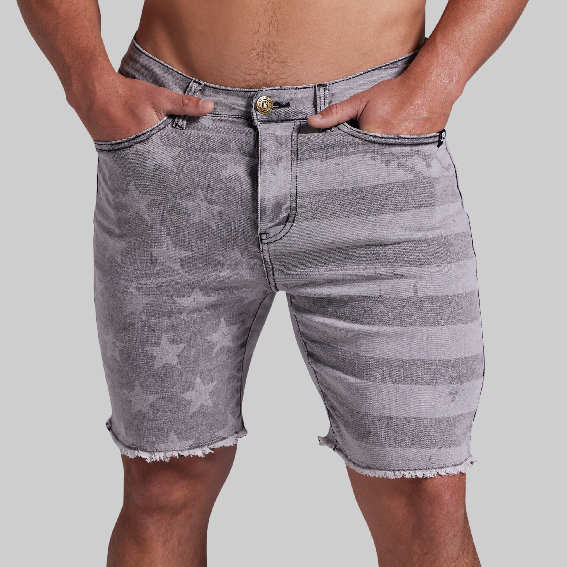 Gray denim shorts with a faded star and stripe pattern, featuring a frayed hem and side pockets, shown on a model against a light gray background.
