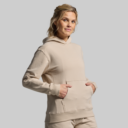Woman wearing a beige hoodie against a plain background