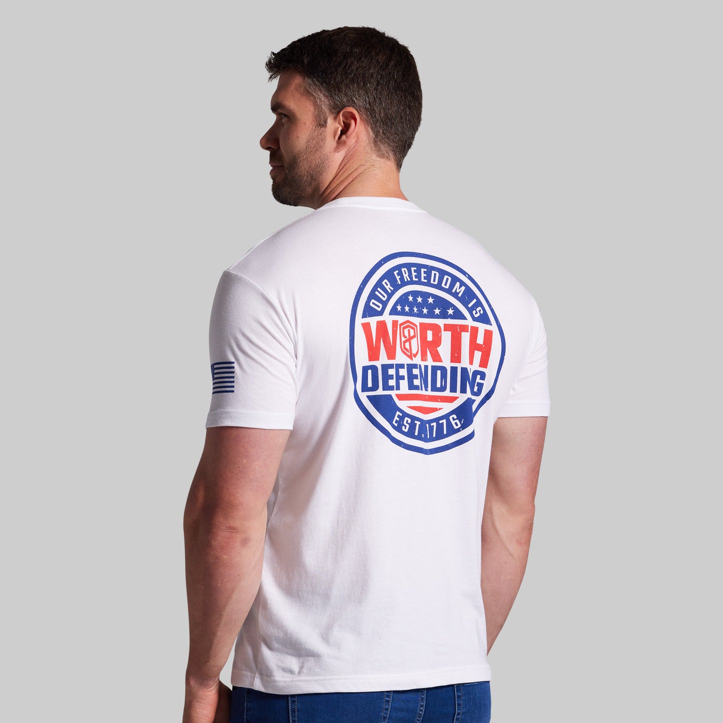 Man wearing a white t-shirt with a logo and text on the back, standing against a plain background