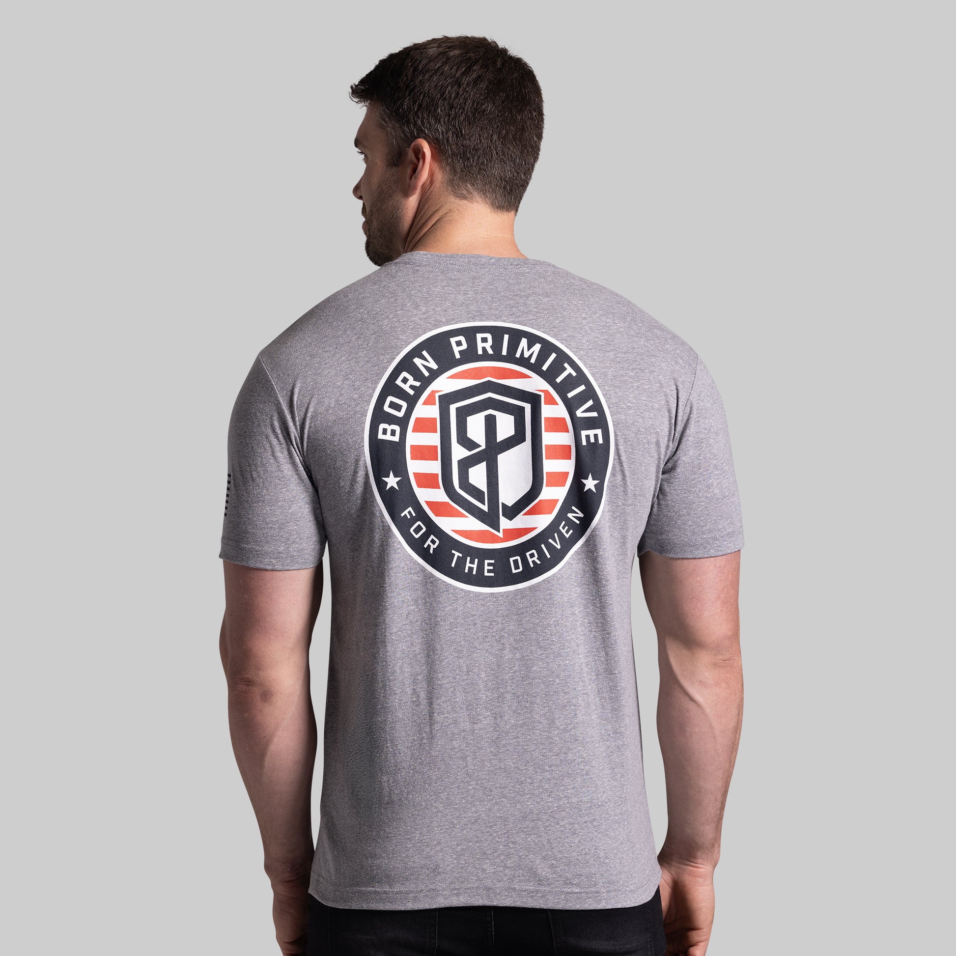 Man wearing a gray t-shirt with 'Born Primitive' logo on the back against a gray background