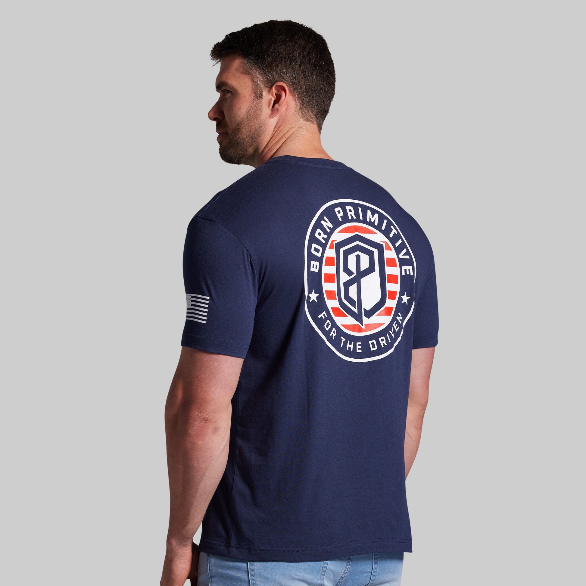 Man wearing a navy blue t-shirt with a logo on the back against a gray background