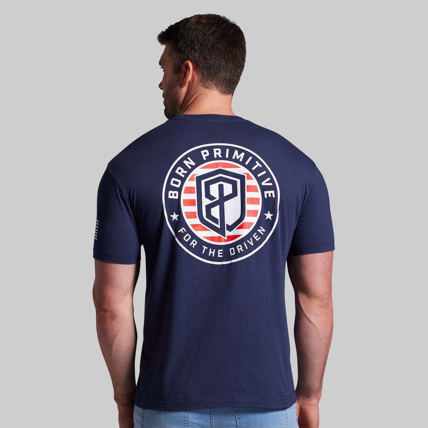 Man wearing a navy blue t-shirt with a logo on the back against a gray background