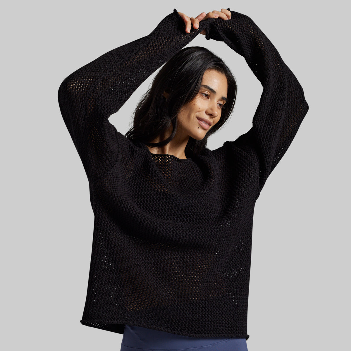A woman modeling a black open-knit long-sleeve sweater against a solid gray background.