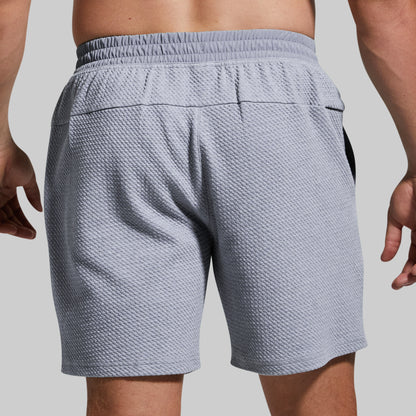 Rear view of a person wearing textured light gray athletic shorts with an elastic waistband and side pockets, shown against a plain light gray background.