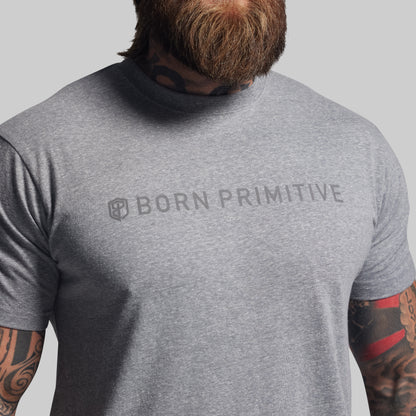Person wearing a gray 'Born Primitive' t-shirt with tattoos visible on arms.