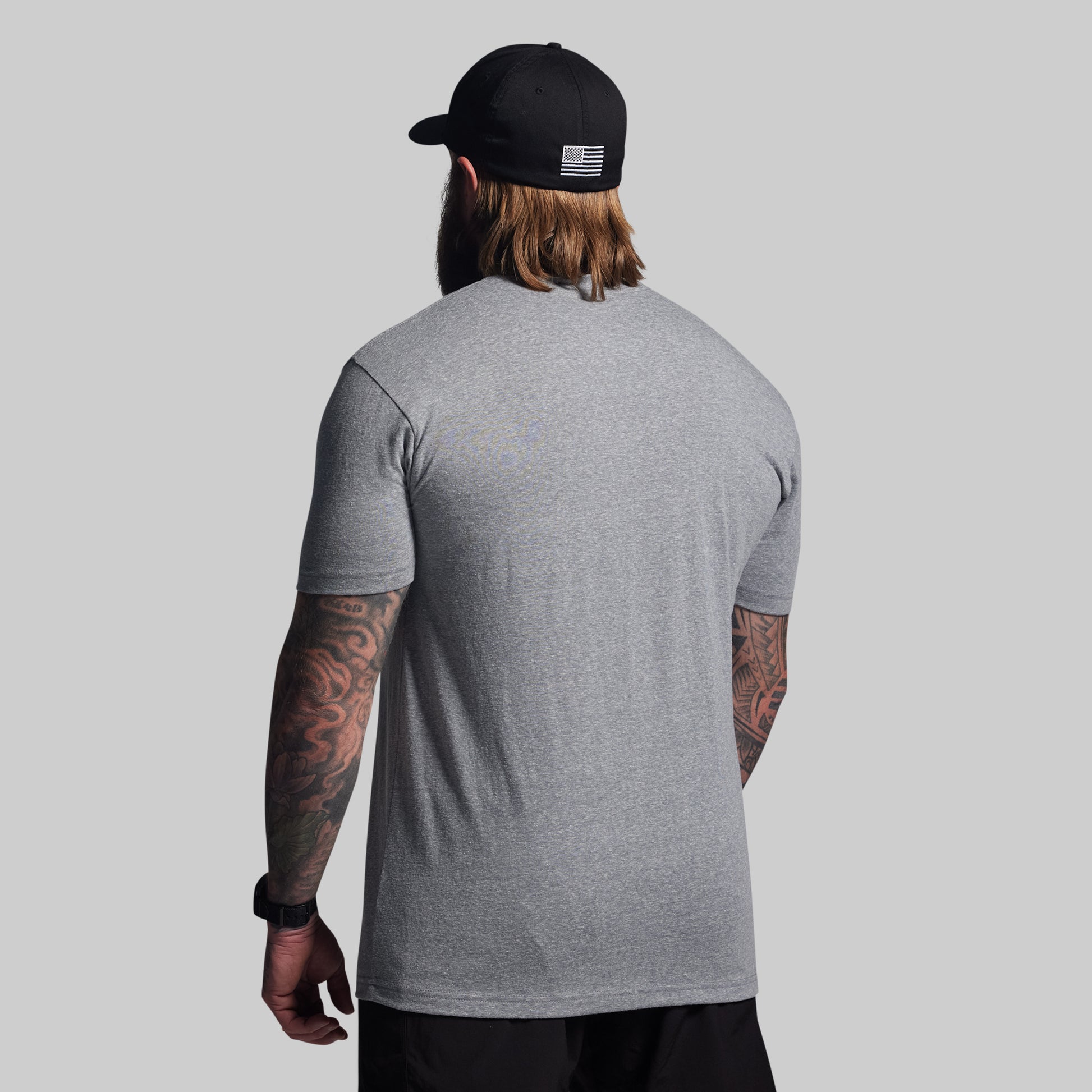 Man wearing a gray t-shirt and black cap with an American flag design on a light gray background