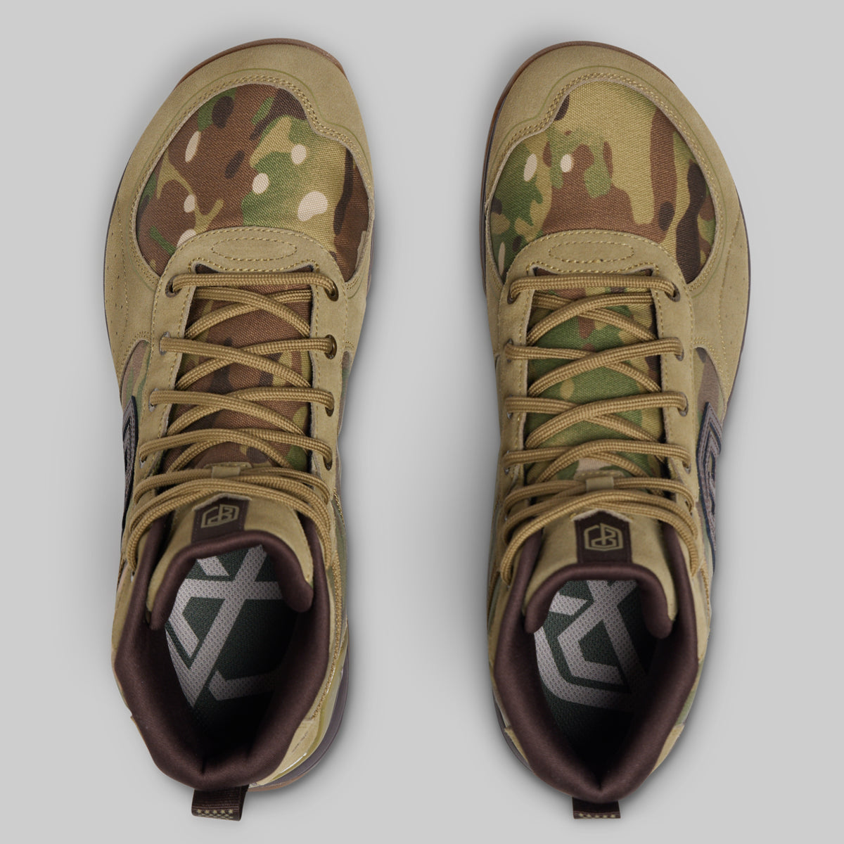 A pair of tactical boots shown from a top-down view, featuring a multi-terrain camouflage pattern in tan, green, and brown, with dark brown laces and a dark interior.