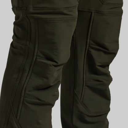 Close-up of dark olive green technical pants showing the leg construction, seam details, and pocket stitching against a neutral gray background.