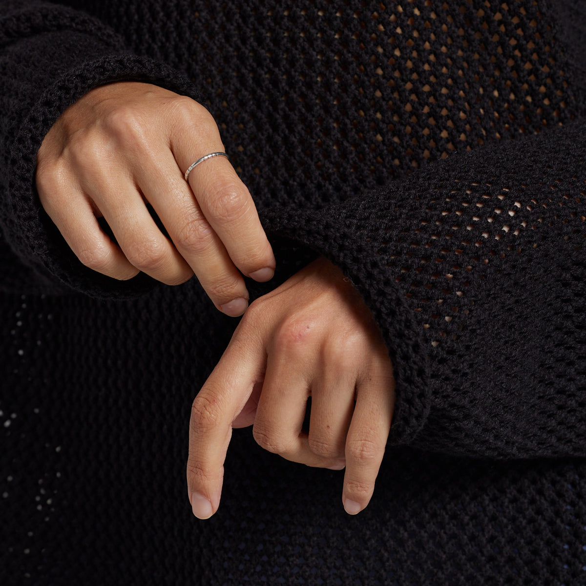 A close-up of a person's hands wearing a black open-knit sweater.