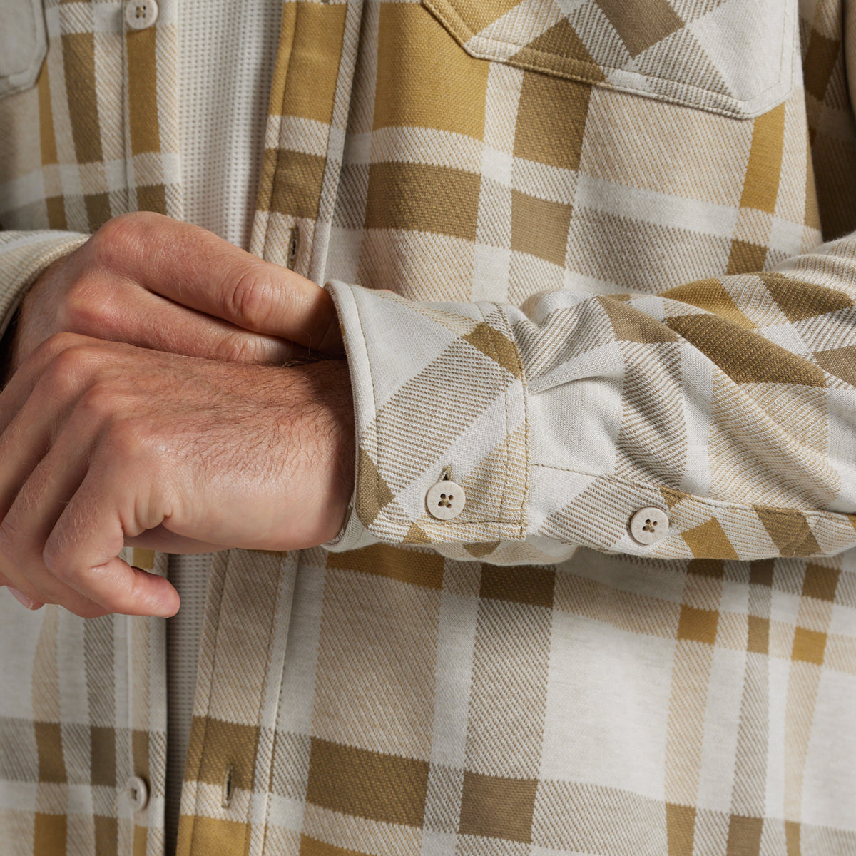 Close-up of a person wearing a long-sleeve plaid flannel shirt, showing the cuff with buttons and the fabric texture.