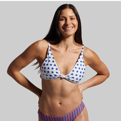 Woman wearing a blue and white star-patterned bikini top and red, white, and blue striped bottom on a gray background