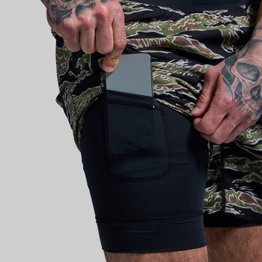 A person wearing camouflage patterned versatile shorts with a compression liner and a phone held in the pocket.