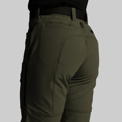 Close-up rear view of olive green outdoor pants worn by a model, showing the back pockets, belt loops, and a small circular logo near the upper right hip, against a light gray background.