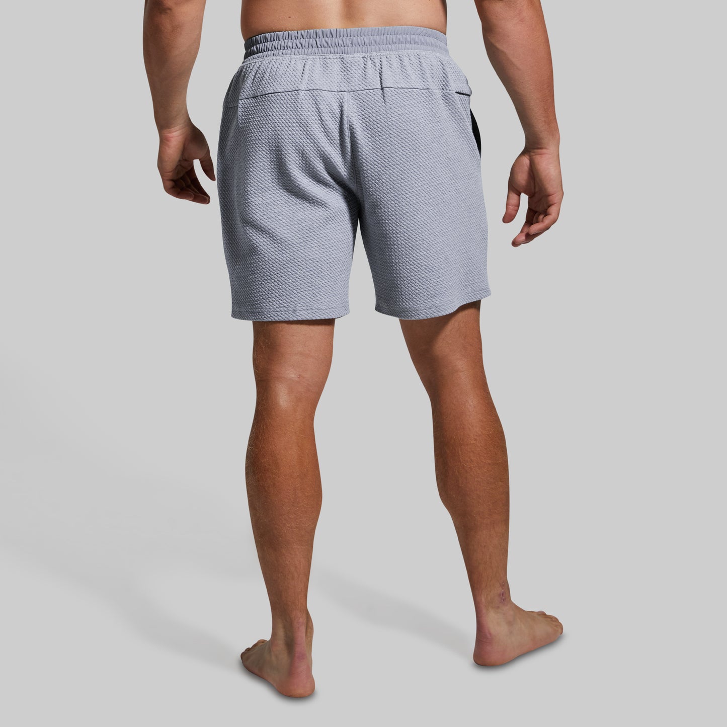 Rear view of a man wearing light gray textured shorts against a solid light gray background.