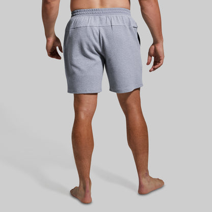 Rear view of a man wearing light gray textured shorts against a solid light gray background.