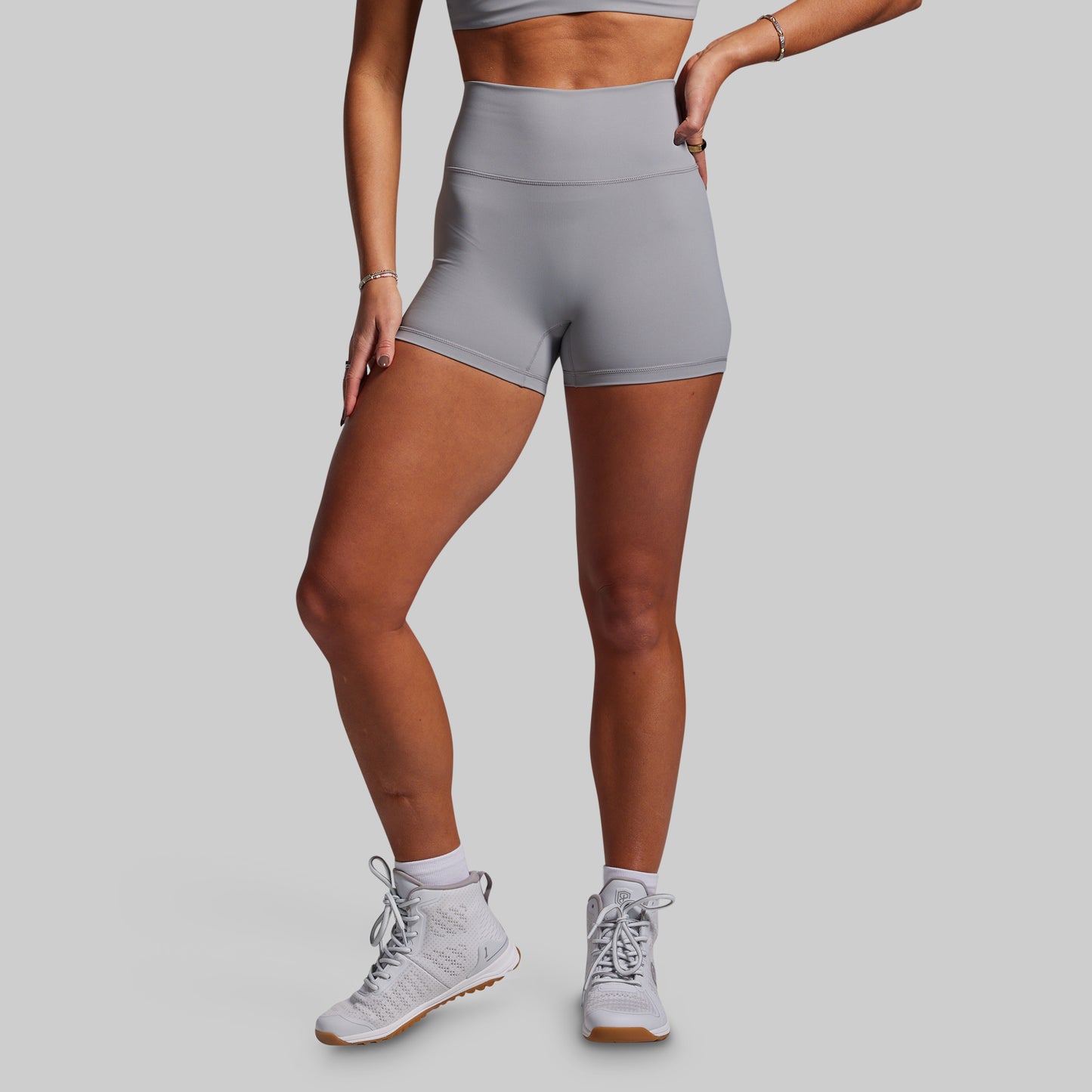 Person wearing gray athletic shorts and white sneakers on a plain background