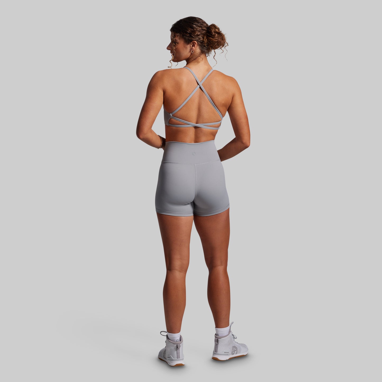 Woman wearing a gray sports bra and shorts set on a plain background