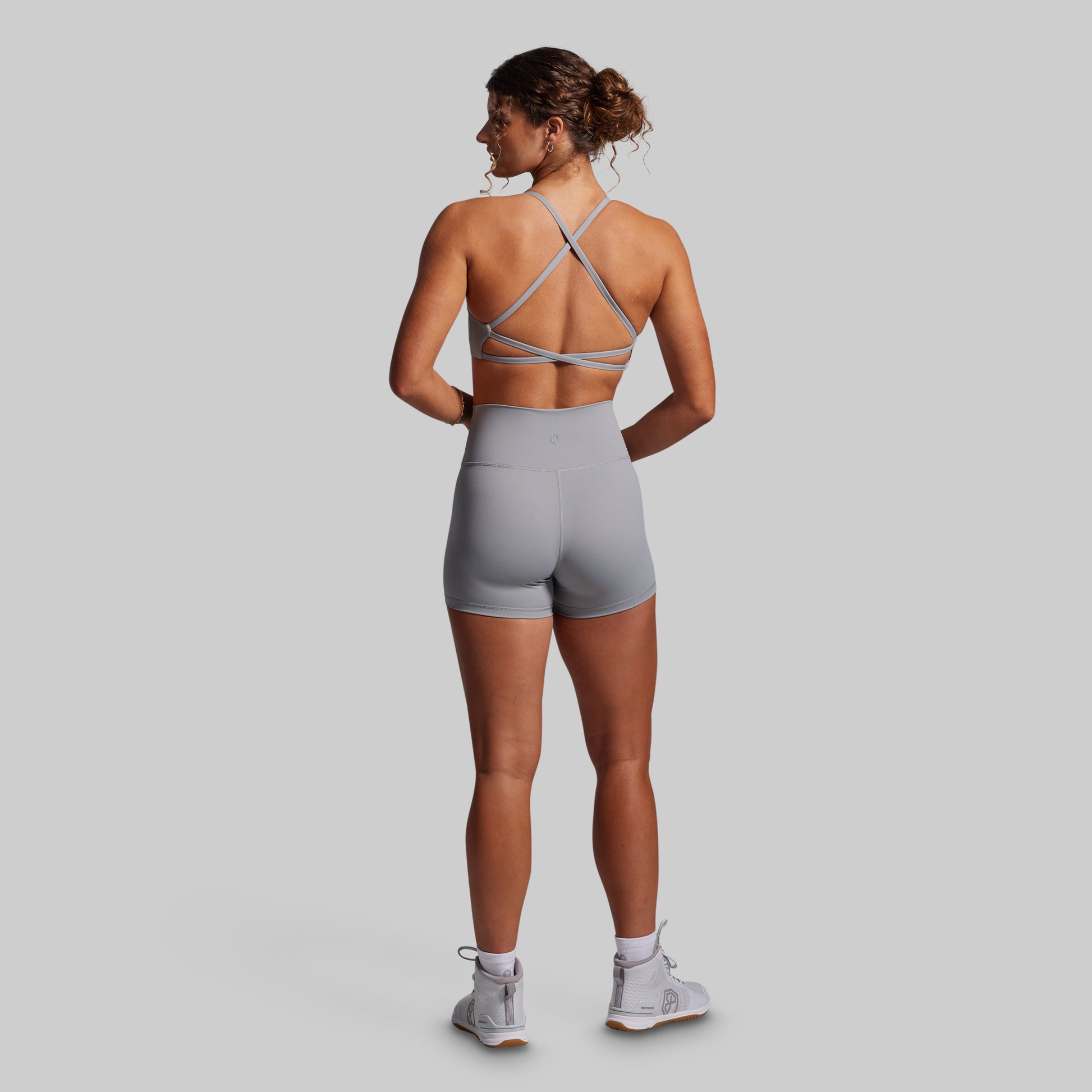 Woman wearing a gray sports bra and shorts set on a plain background