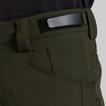 Close-up of the back waistband and pocket area of olive green outdoor pants, showing a black hook-and-loop patch with a silver metal bar, stitching, and belt loops.