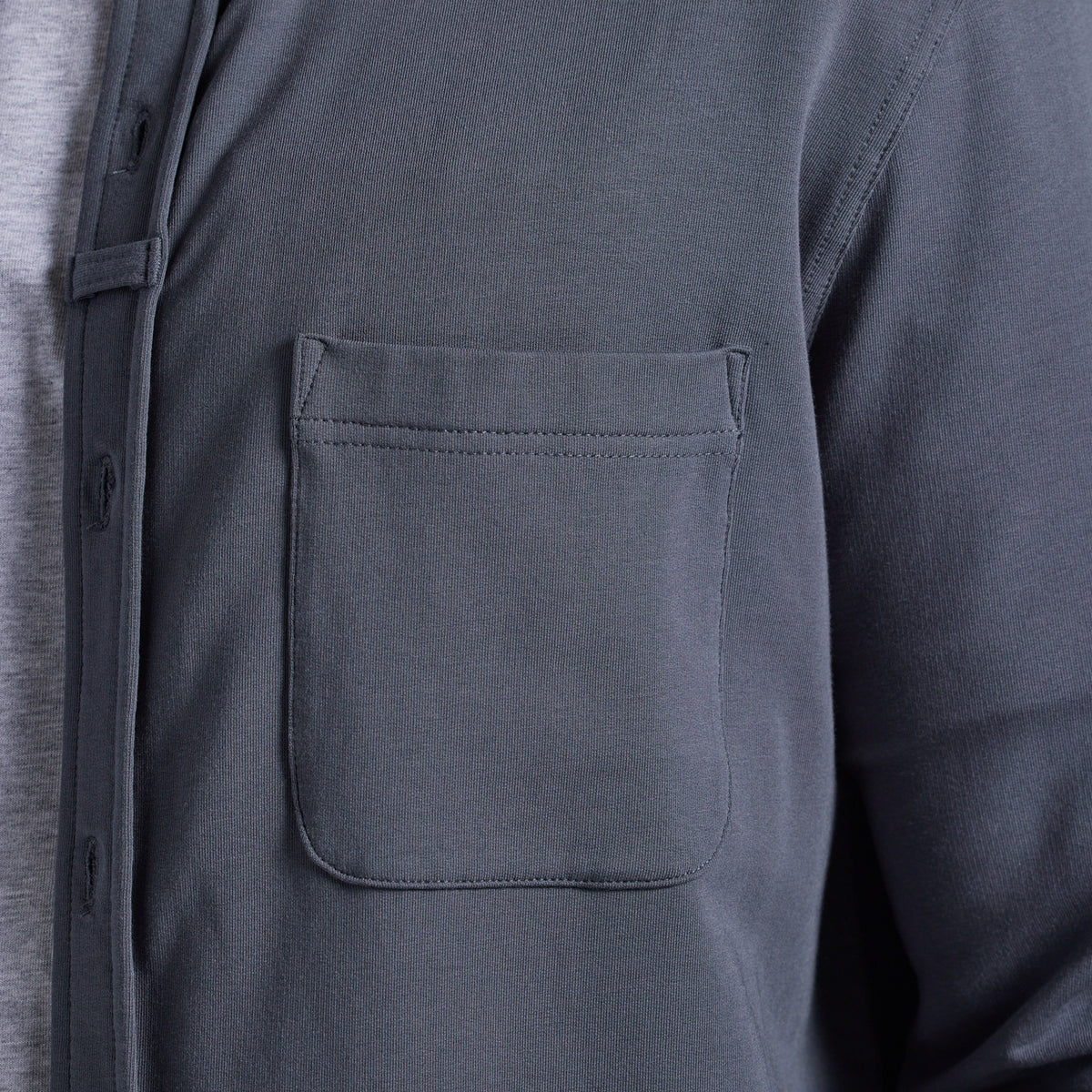 Close-up of a dark gray long-sleeve button-up shirt with a chest pocket, worn over a light gray undershirt.