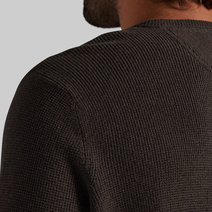 Close-up back view of a person wearing a dark brown ribbed knit sweater, showing the shoulder and upper back against a light gray background.
