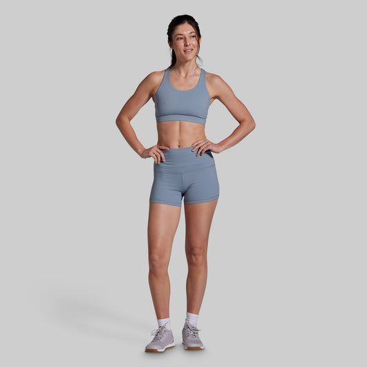 Woman wearing a gray sports bra and shorts on a light gray background