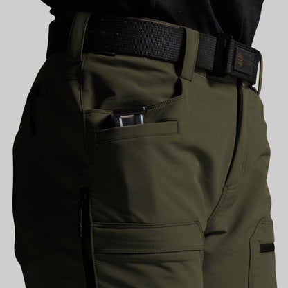 Close-up of olive green outdoor cargo pants with a black web belt, showing a side pocket holding a phone and other cargo pockets, on a light gray background.