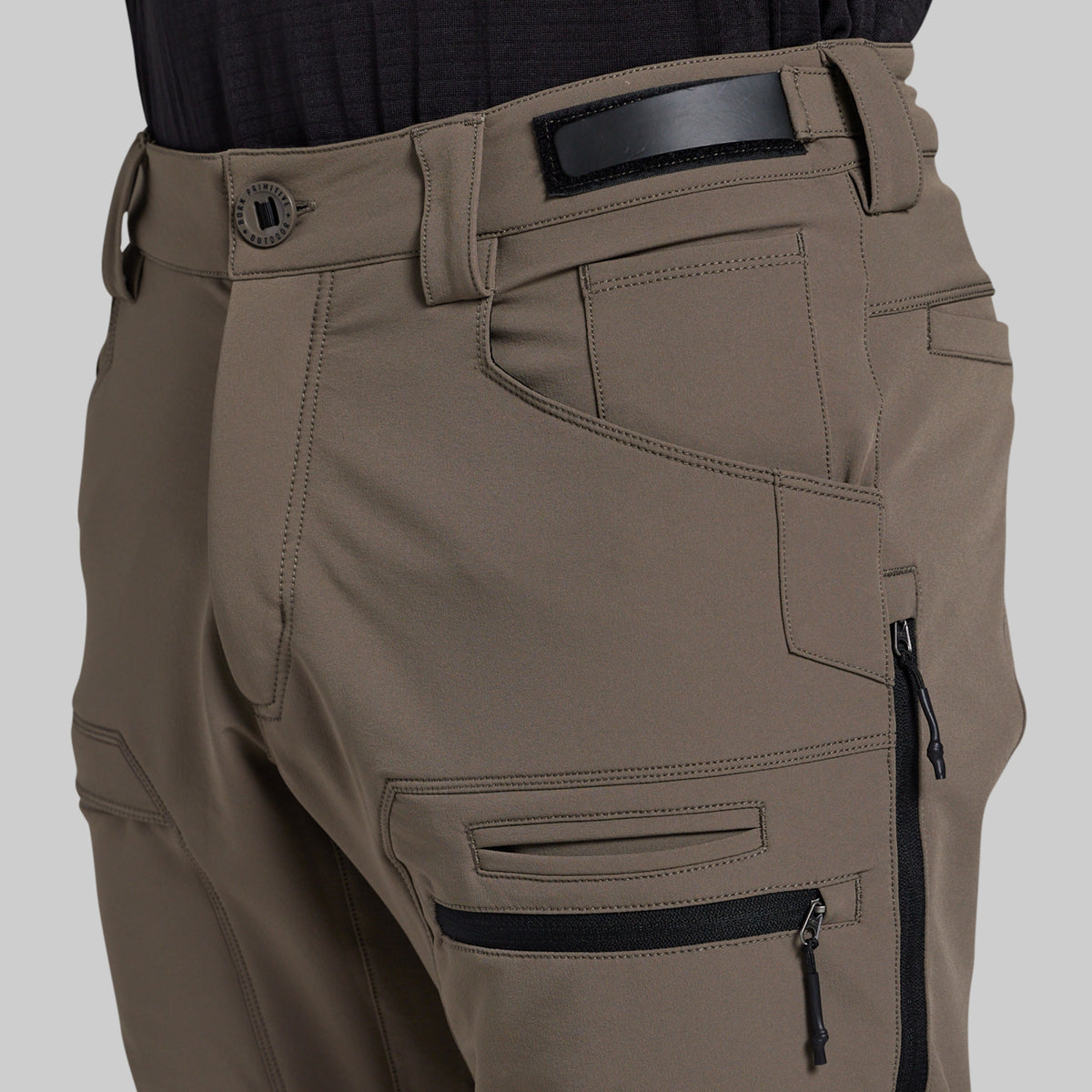 Close-up of a person wearing outdoor cargo pants in a storm grey color, featuring a black belt, belt buckle, and multiple zippered pockets.
