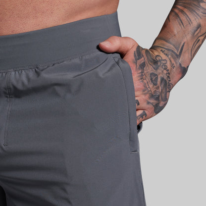Person wearing gray shorts with a tattooed arm on a light gray background