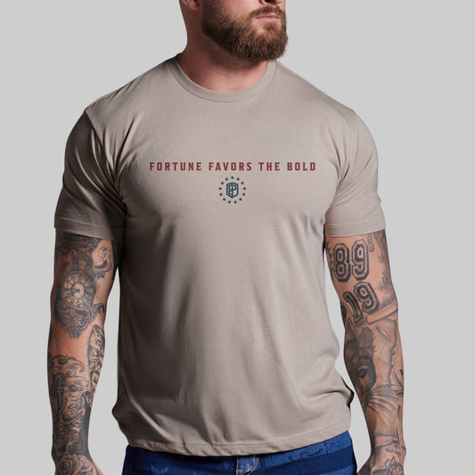 Man wearing a beige t-shirt with 'Fortune Favors the Bold' text and logo on a plain background