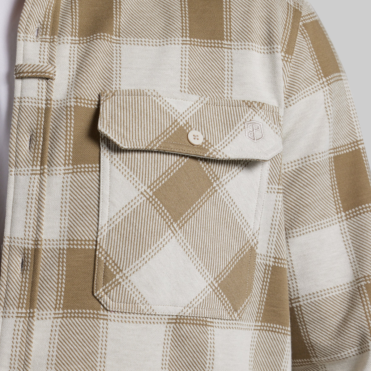 Close-up of a plaid button-up shirt with a chest pocket, featuring a tan and off-white check pattern.